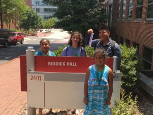 Youth posing by NC State's Riddick Hall sign.