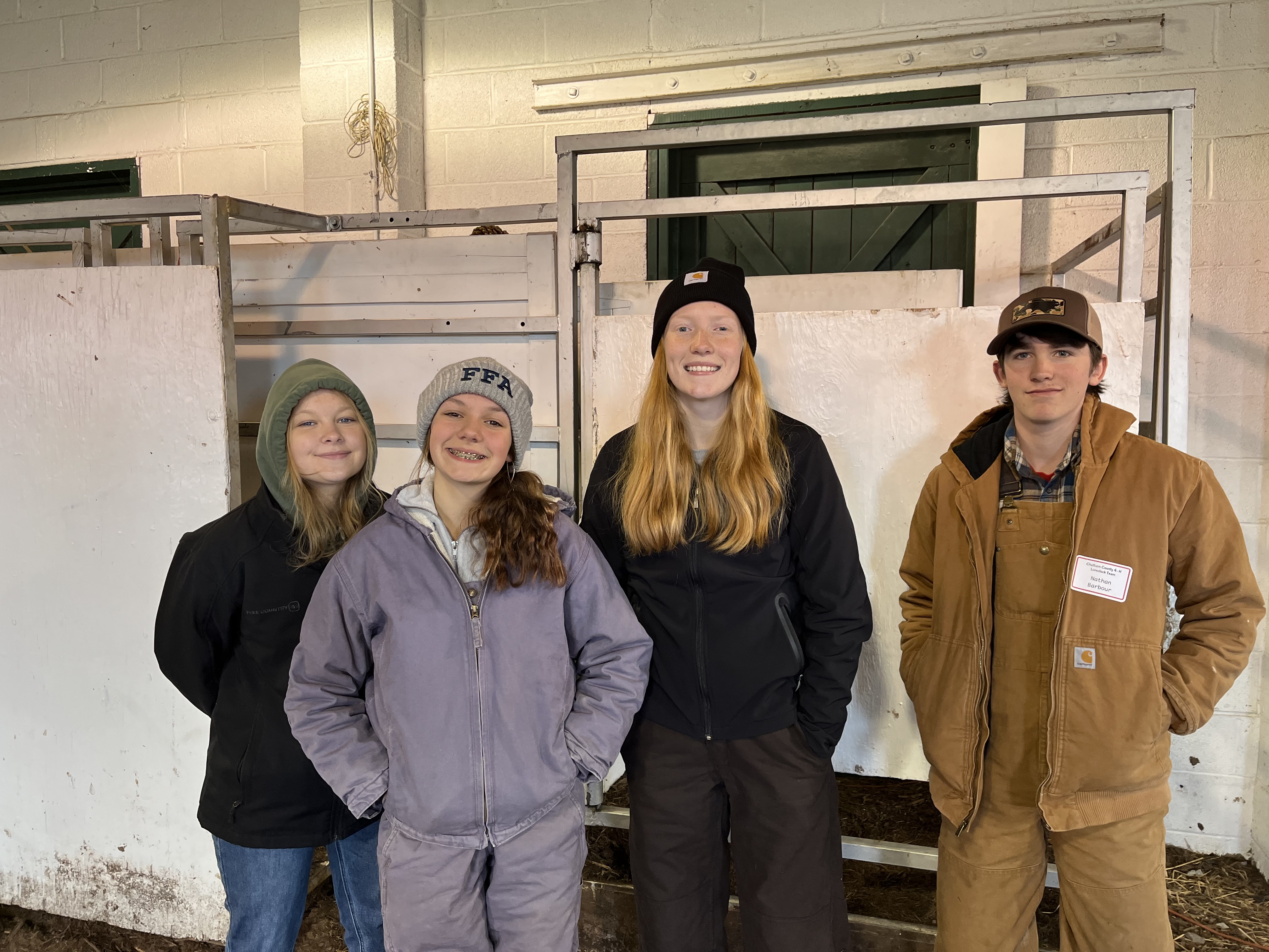 Four teenagers pose in front of a metal structure in a barn.