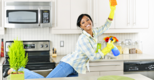 Person leaping in kitchen while holding a sponge and cleaning products.