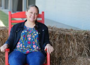 CRD/4-H Extension Agent, Rachael Blazzard sits in red chair in front of straw bales